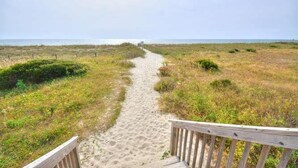 Un sentier sablonneux menant à la plage, avec une rambarde en bois d’un côté.