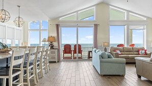 Un salón espacioso con vistas al océano, un comedor con sillas y una mesa, y una zona de estar con sofá y sillones.