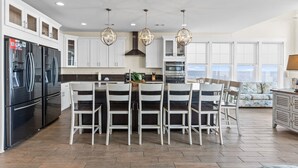 Una cocina moderna con armarios blancos, una isla central con sillas, electrodomésticos de acero inoxidable e iluminación colgante.
