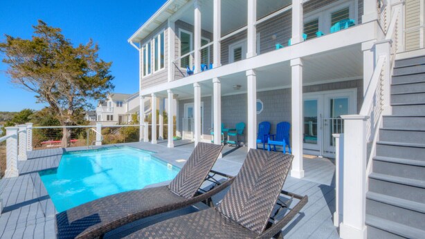 Ein Poolbereich mit Liegestühlen, einem Schwimmbecken und einer überdachten Terrasse.