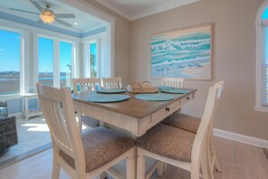 Un coin repas avec une table en bois, des chaises blanches et un ventilateur de plafond.