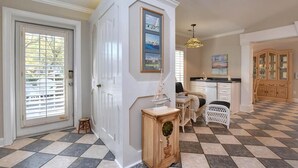 Um quarto espaçoso com piso xadrez, uma porta branca, um banquinho pequeno, um armário de madeira e um espaço de jantar com mesa e cadeiras.