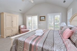 A bedroom with a large bed, a wardrobe, a chair, and a window with blinds.