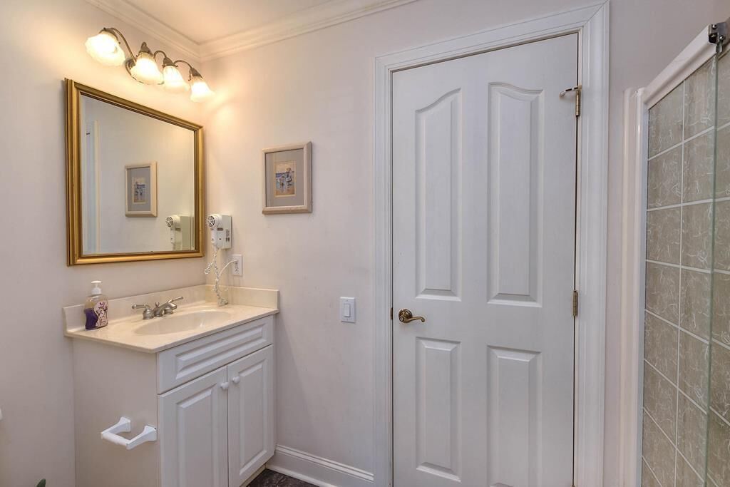 Un baño con tocador blanco, un espejo grande y una puerta con cabina de ducha de vidrio.