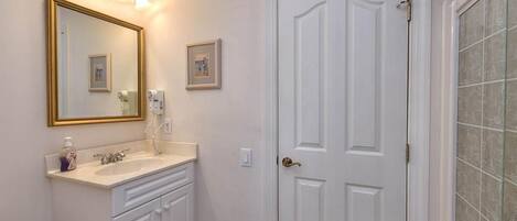 Un baño con tocador blanco, un espejo grande y una puerta con cabina de ducha de vidrio.