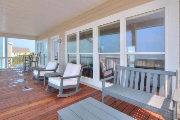 A covered outdoor area with wooden flooring, white rocking chairs, and a bench.