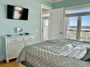 Quarto com cama, penteadeira, televisão e porta que dá para uma varanda com vista.