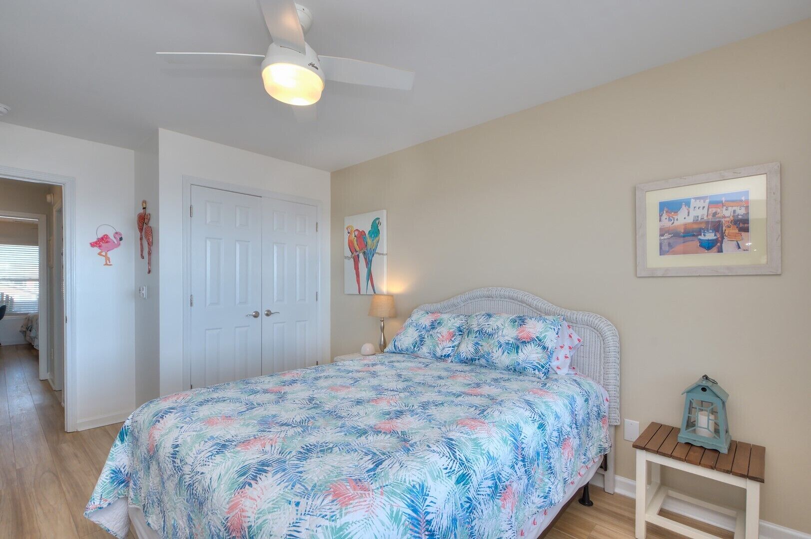 A bedroom with a bed, a ceiling fan, a nightstand, a framed picture, and a small table with a lantern.
