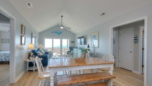 A spacious room with a wooden dining table, white chairs, a blue sofa, and a ceiling fan. - The Jolly Rogers: Oceanview house in Oak Island with private pool and spacious layout. (Oak Island)