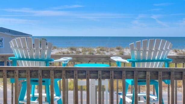 A wooden deck with two turquoise Adirondack chairs and a small round table, overlooking a beach and ocean. - The Jolly Rogers: Oceanview house in Oak Island with private pool and spacious layout. (Oak Island)