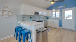 A modern kitchen with white cabinets, a blue accent wall, and a kitchen island with stools. - The Jolly Rogers: Oceanview house in Oak Island with private pool and spacious layout. (Oak Island)