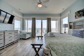Un dormitorio con una cama grande, un escritorio, una silla, un televisor y vistas a la playa.
