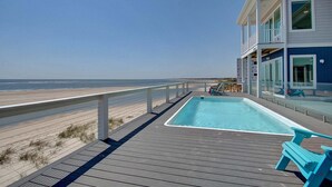 Un espace aménagé au bord de la piscine, avec vue sur la plage, une terrasse et un bâtiment doté de balcons.