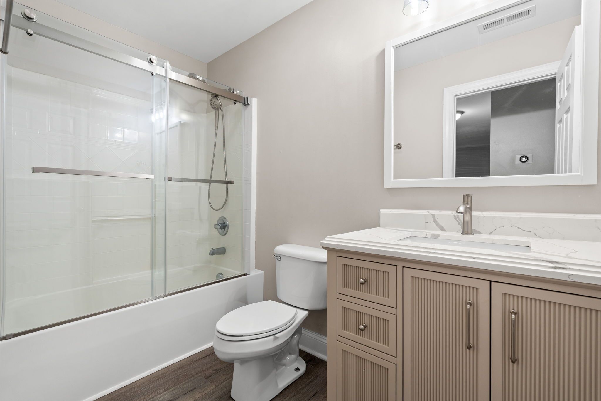 A bathroom with a glass-enclosed shower, a toilet, and a vanity with drawers.
