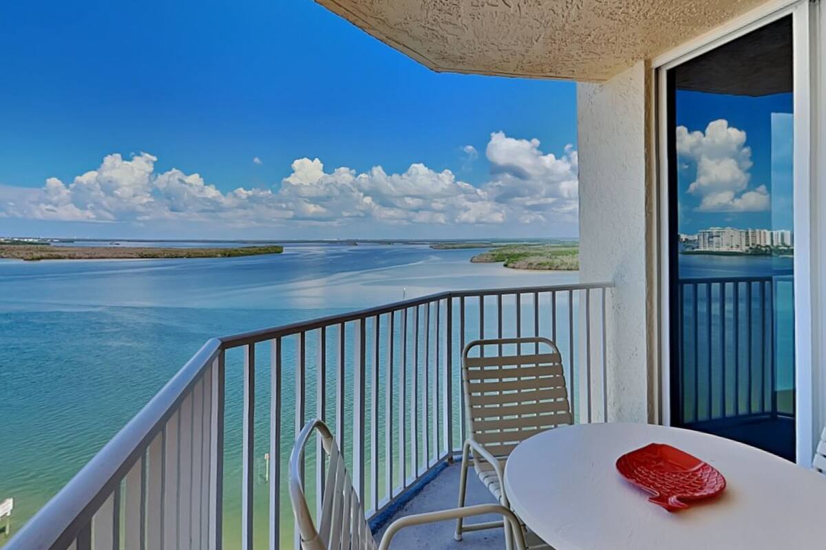 A balcony with a view of a calm sea and distant buildings.