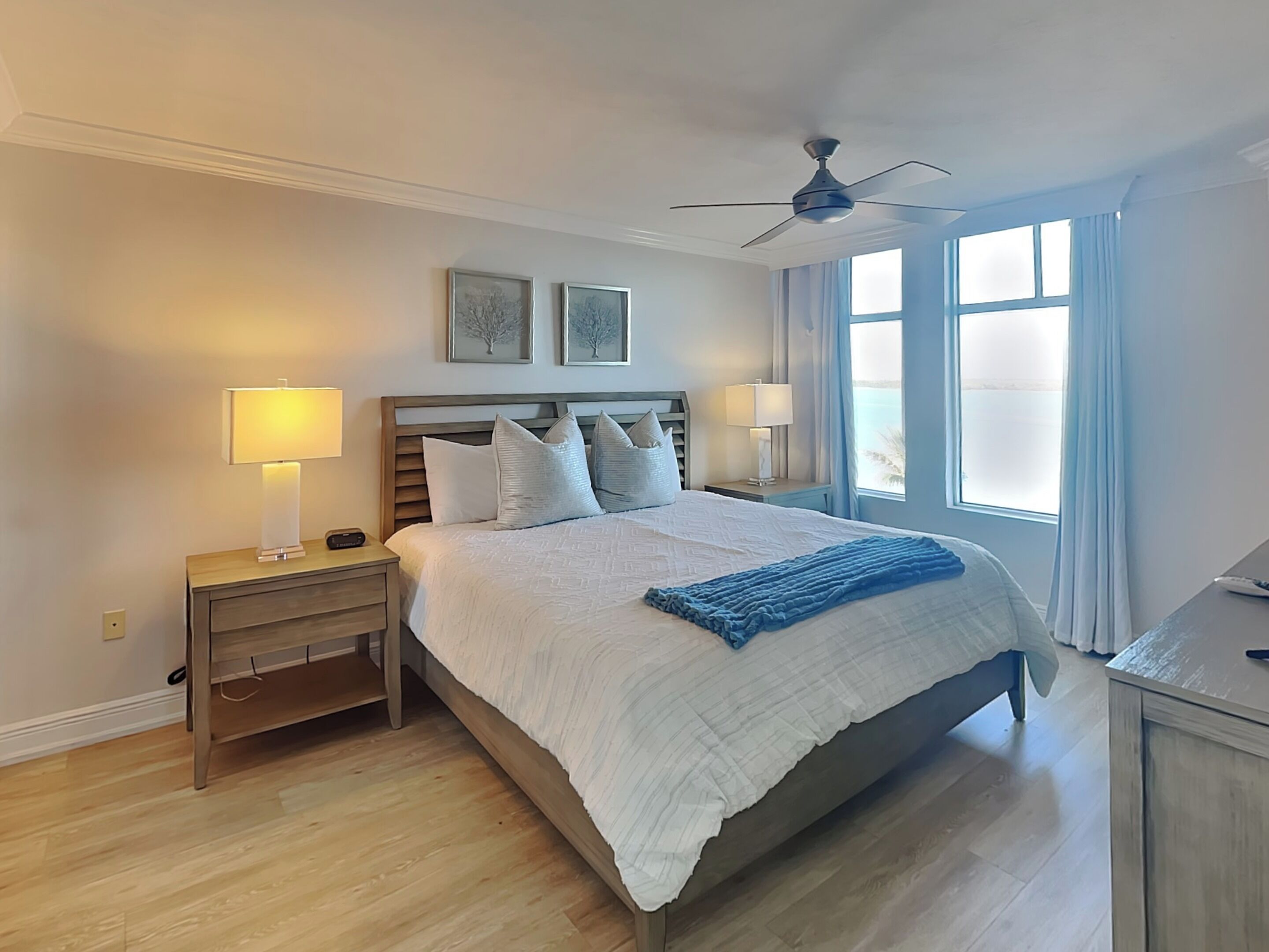 Ein Schlafzimmer mit einem großen Bett, zwei Nachttischen mit Lampen, einem Deckenventilator und einem Fenster mit Vorhängen.