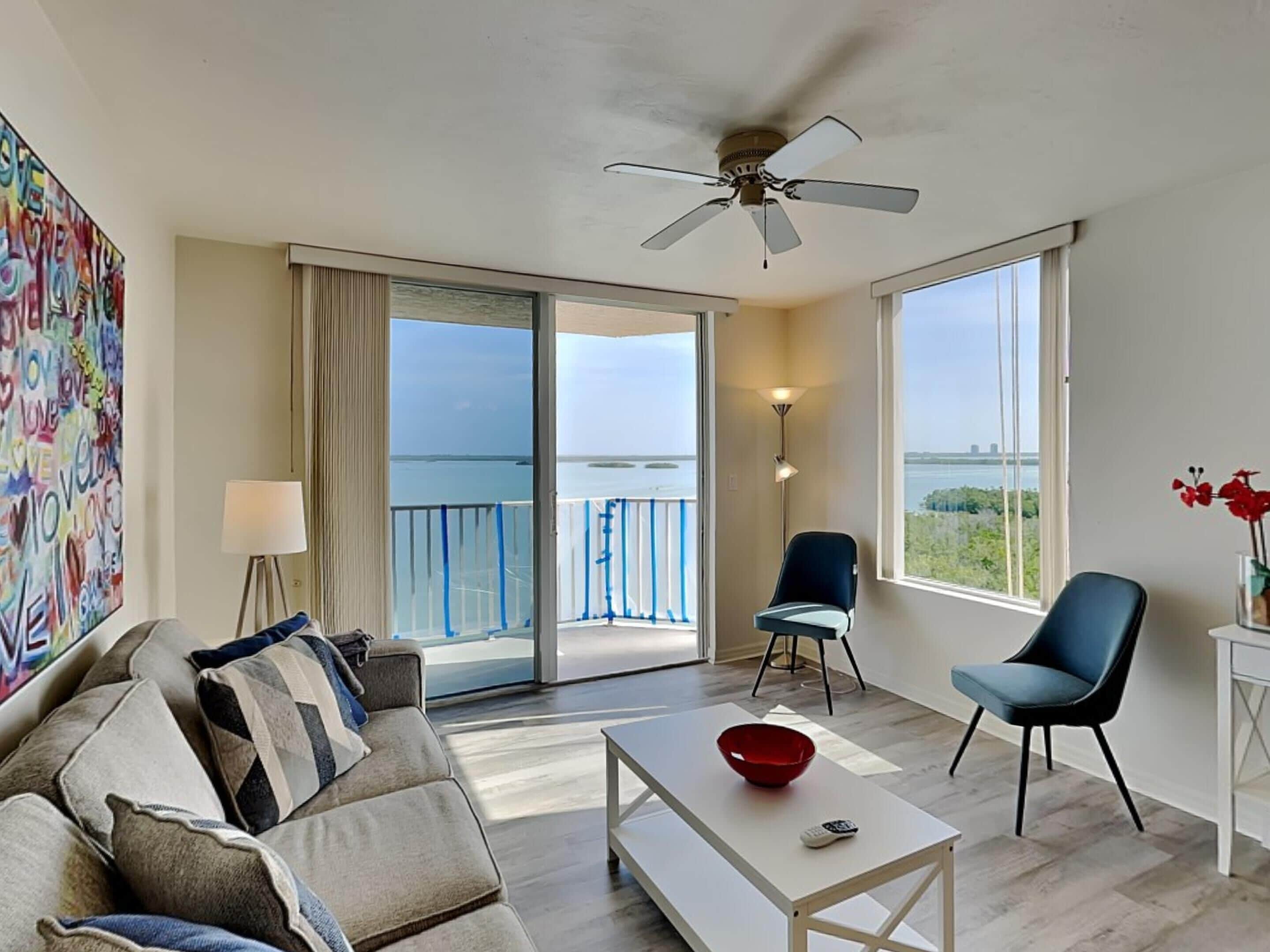 A modern living room with a sofa, chairs, a coffee table, and a balcony with a view of the sea.