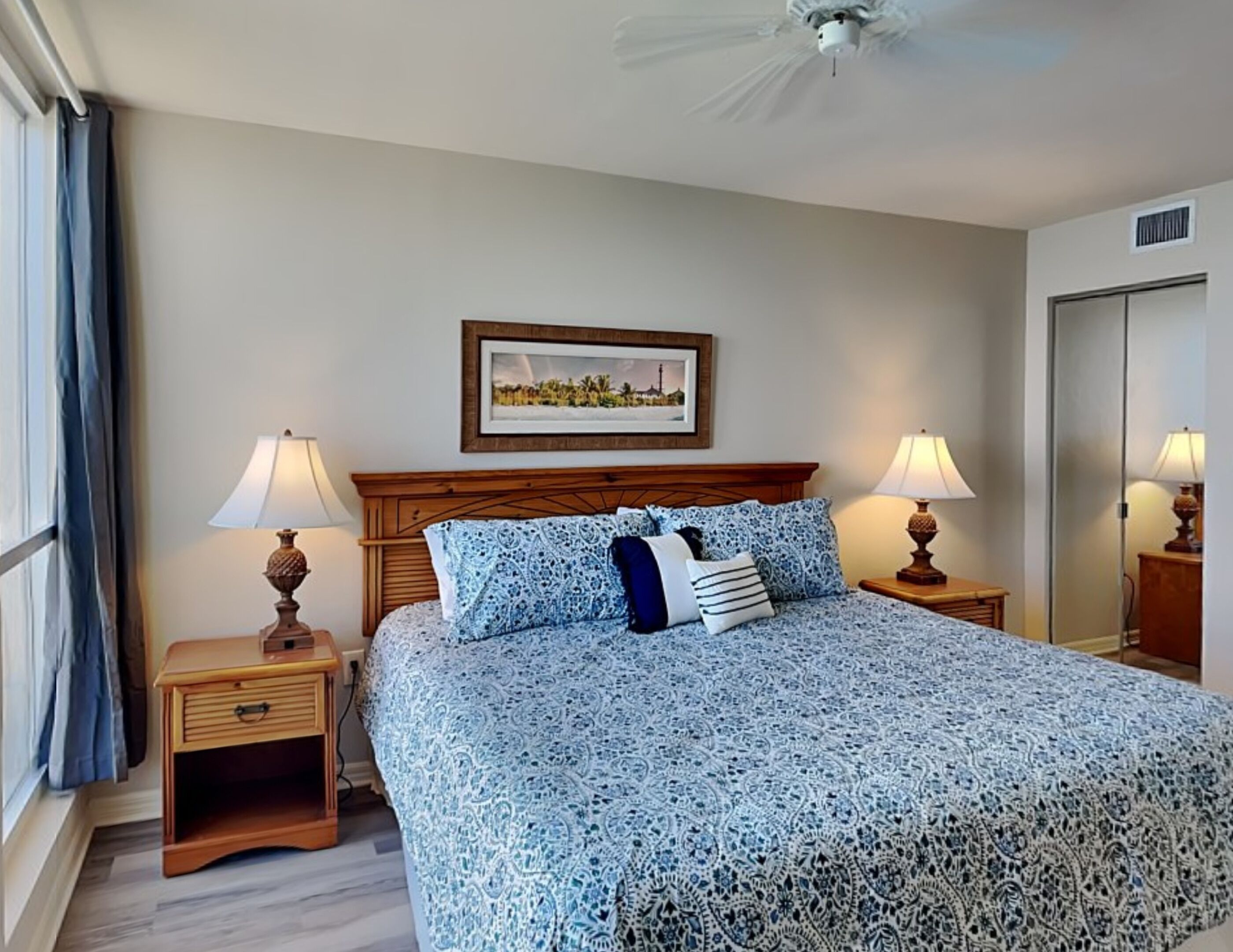 A hotel room with a bed, two bedside tables with lamps, a framed picture on the wall, and a ceiling fan.
