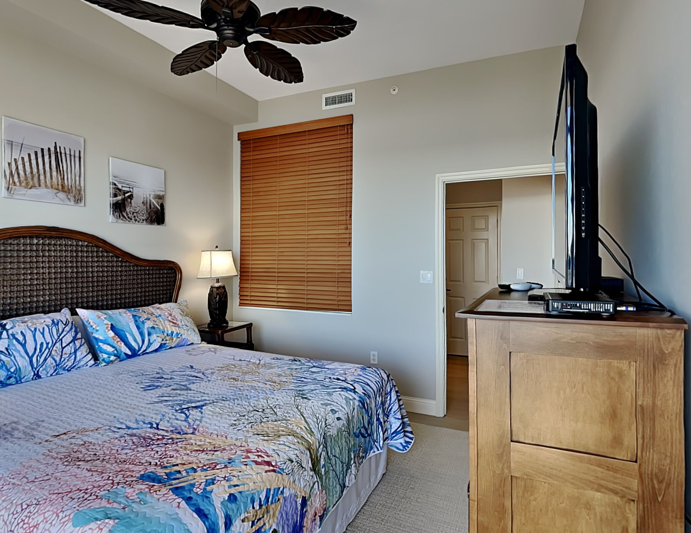 A bedroom with a bed, a wooden dresser, a ceiling fan, and a television.