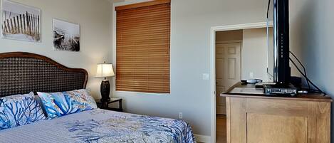 A bedroom with a bed, a wooden dresser, a ceiling fan, and a television.