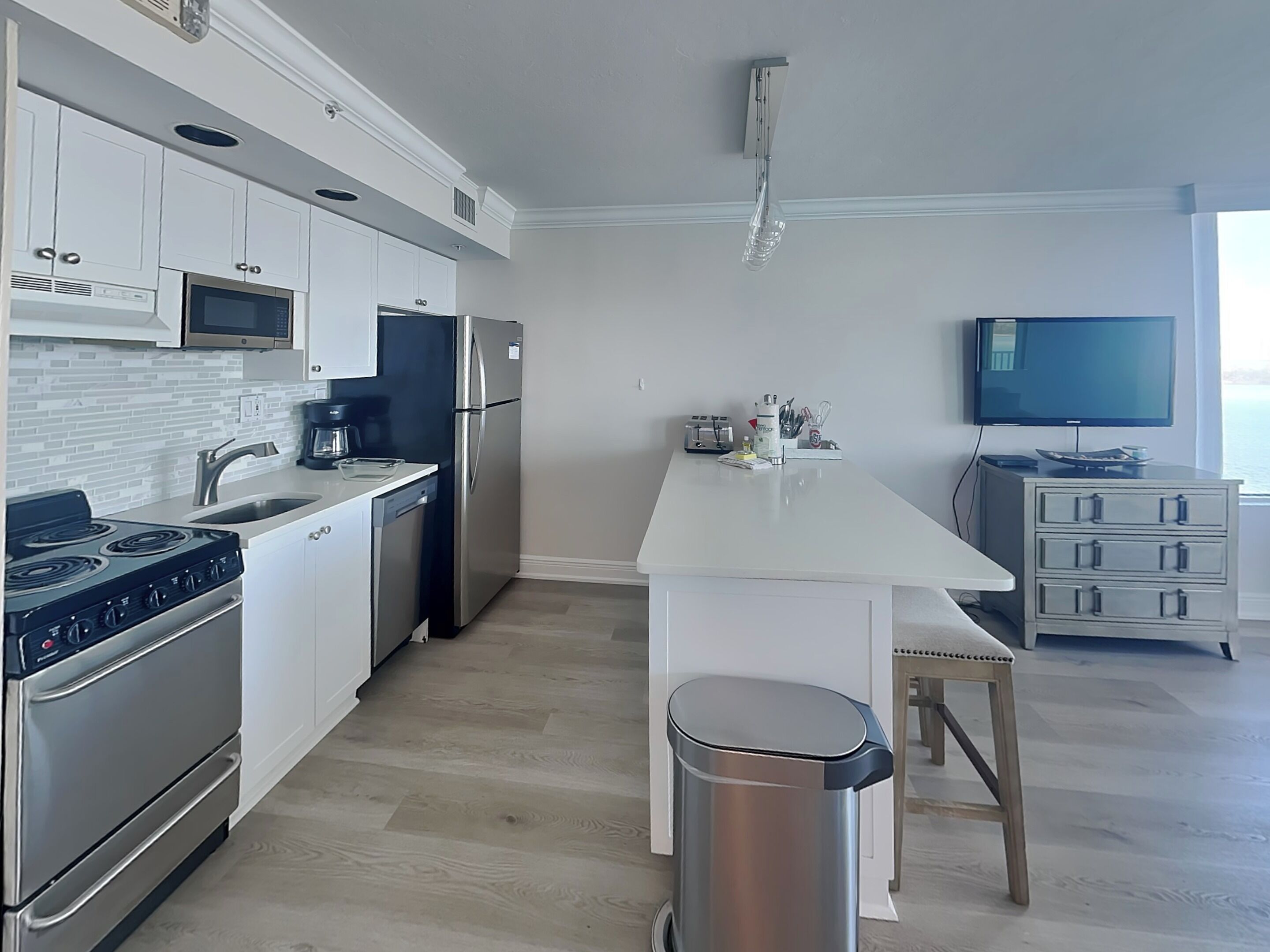 A modern kitchen with white cabinetry, stainless steel appliances, a central island, and a TV mounted on the wall.