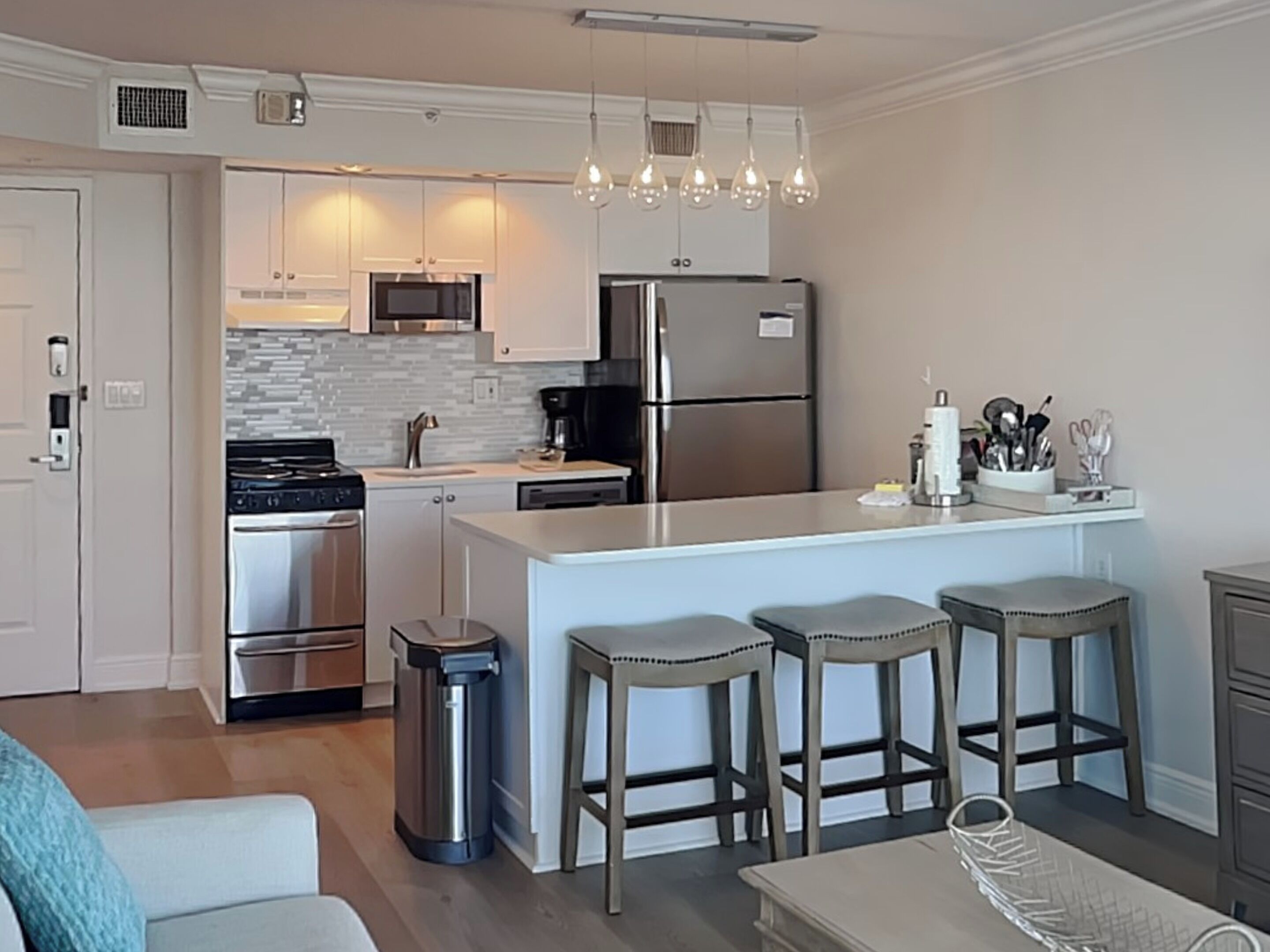 A modern kitchen with stainless steel appliances, a central island with bar stools, and pendant lighting.