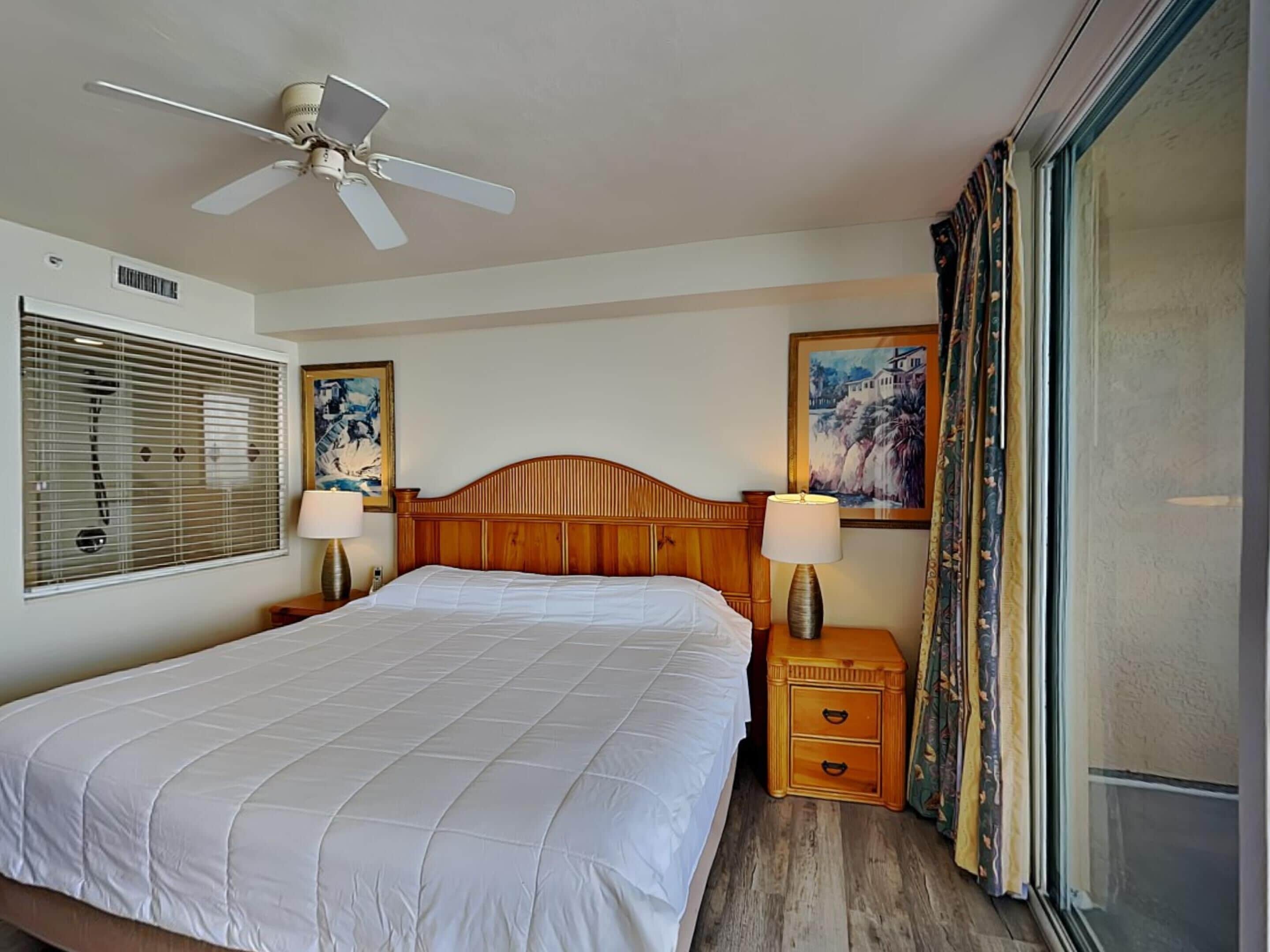 A hotel room with a large bed, a ceiling fan, two bedside lamps, a wooden nightstand, and a window with curtains.