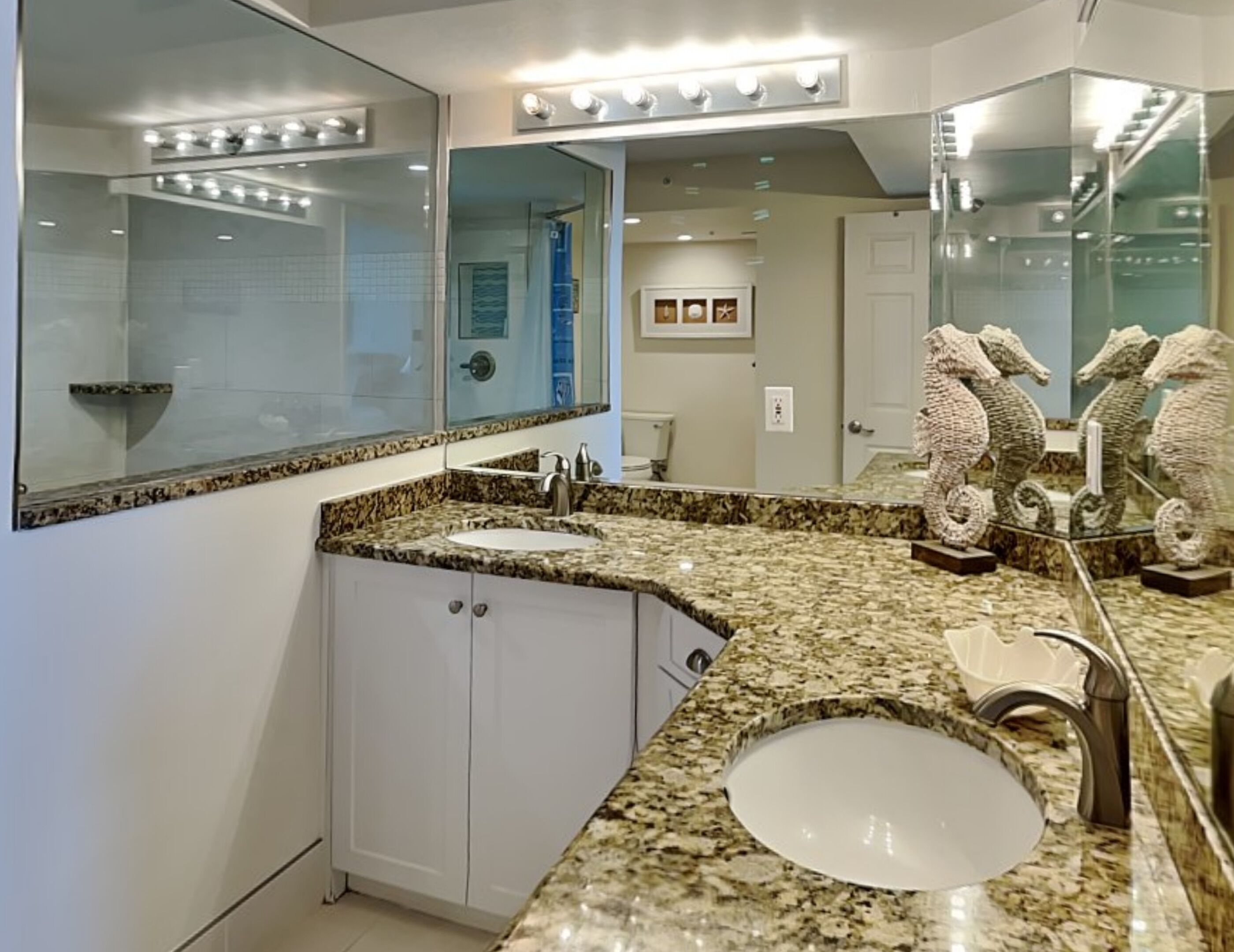 Une salle de bain avec un comptoir en granit, un lavabo et un grand miroir avec éclairage intégré. On y trouve également des statues de chevaux décoratives et une horloge au mur.