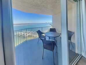 Un balcon avec une table et des chaises, donnant sur une étendue d’eau et une côte lointaine.