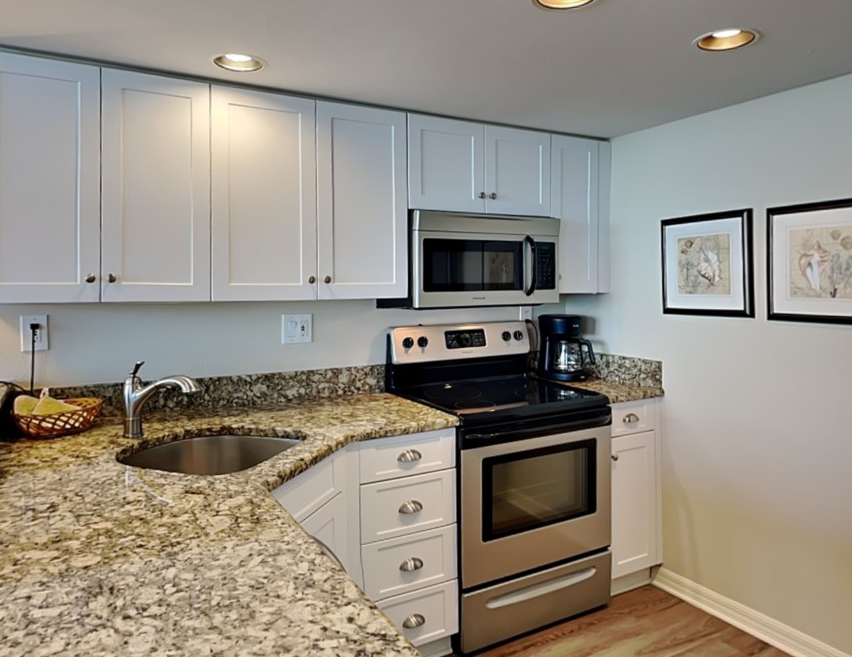 A kitchen with white cabinets, a granite countertop, a stainless steel stove, a microwave, and a coffee maker.