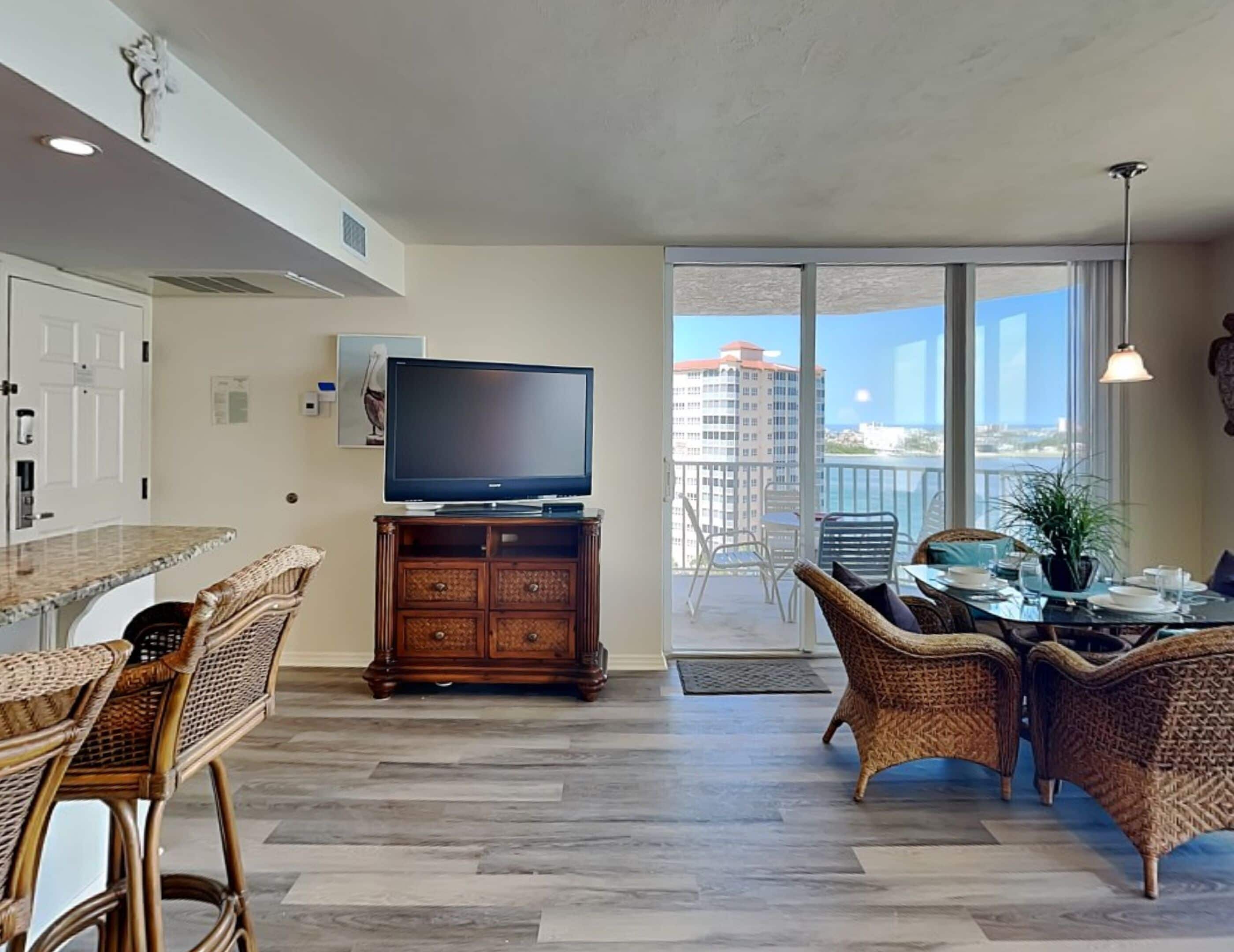 A modern living room with a flat-screen TV, wicker furniture, and a balcony with a city view.