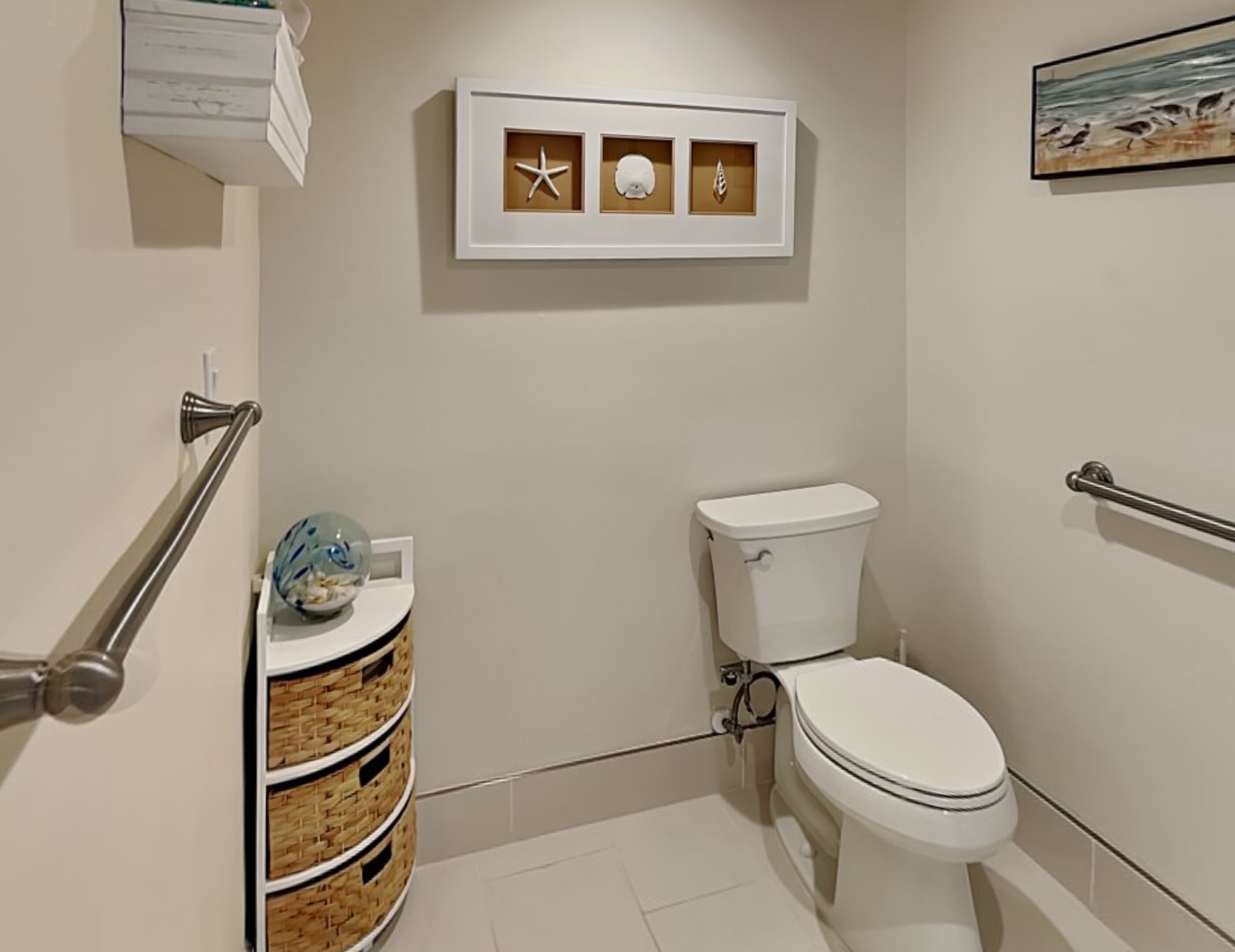 Un baño con inodoro, un mueble de pared con objetos decorativos, un pasamanos y una cesta con un globo terráqueo.