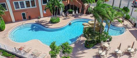 A rooftop swimming pool with lounge chairs and palm trees, surrounded by a multi-story building.