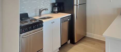 A compact kitchen with a stove, microwave, sink, and refrigerator.