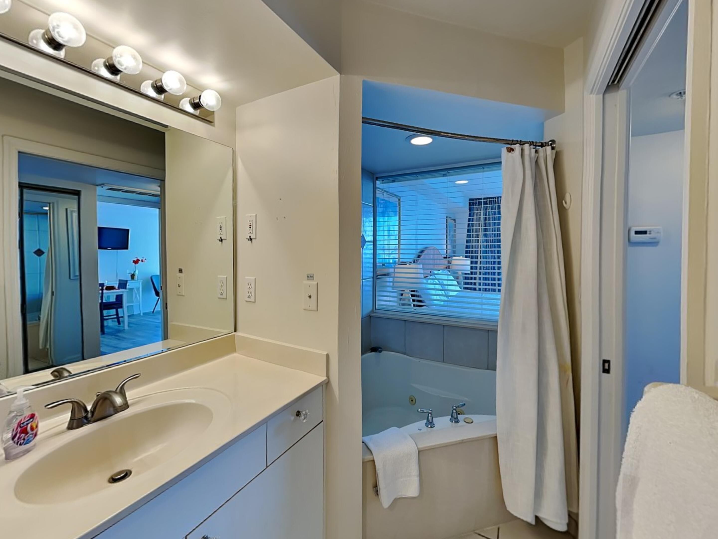 A modern bathroom with a large mirror, vanity, sink, and bathtub.