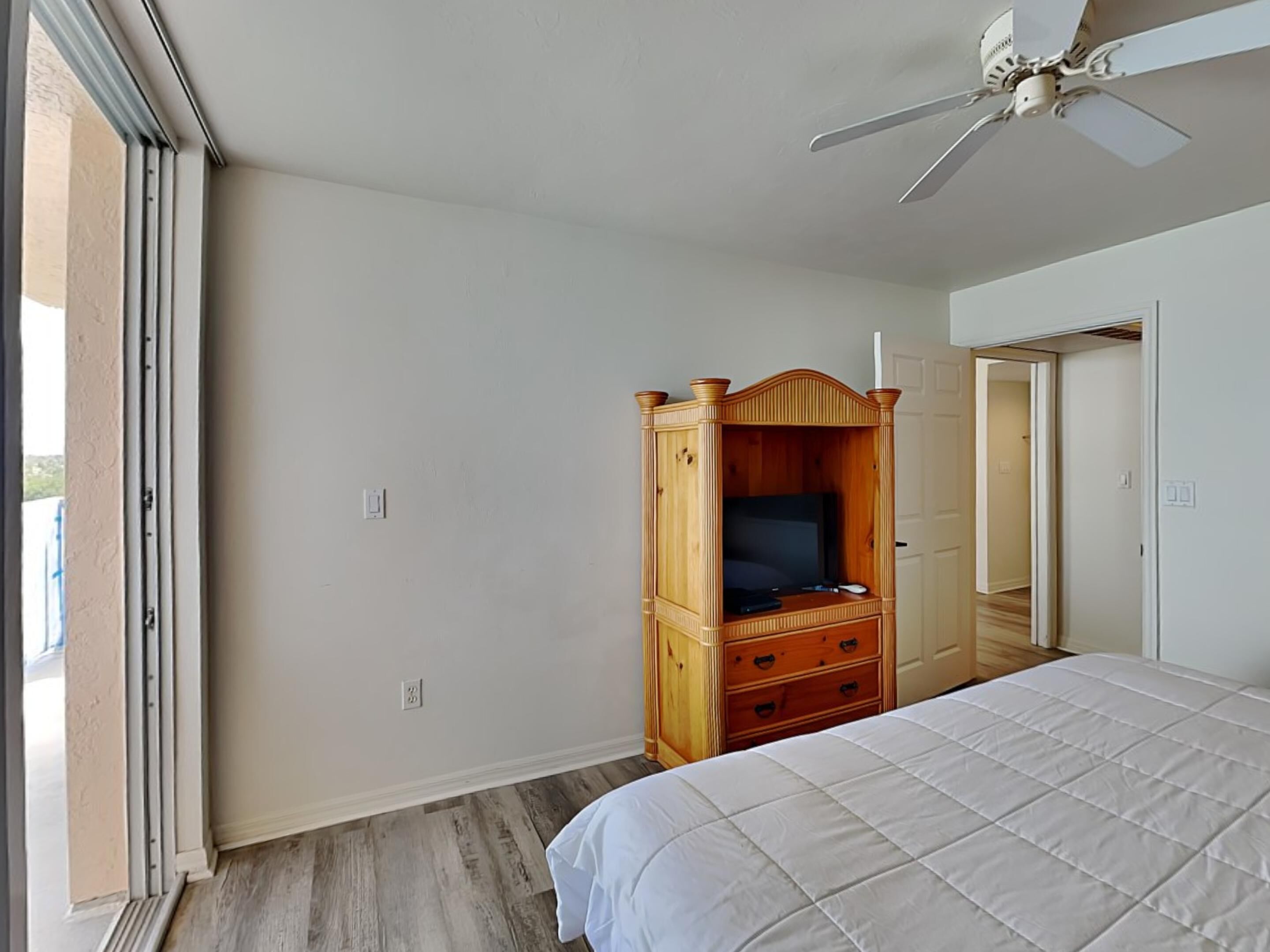 Ein Schlafzimmer mit einem Bett, einem Holzschrank, einem Deckenventilator und einer Tür zu einem anderen Raum.