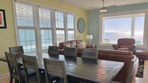 A dining area with a table and chairs, a sofa, and a view of the ocean. - Discover Zion in Oak Island: an oceanfront dream with 5 bedrooms for 12 guests! (Oak Island)