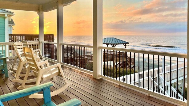 A covered deck with rocking chairs, a view of the ocean, and a gazebo. - Discover Zion in Oak Island: an oceanfront dream with 5 bedrooms for 12 guests! (Oak Island)