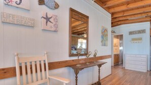 A room with a wooden ceiling, a wooden-framed mirror, a wooden table, and a white chair with a patterned cushion. - Oceanfront haven in Oak Island—spacious 3BR, 2BA home for up to 8 guests! (Oak Island)