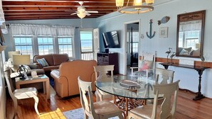 A spacious living area with a glass dining table, wooden ceiling, and a view of the ocean through large windows. - Oceanfront haven in Oak Island—spacious 3BR, 2BA home for up to 8 guests! (Oak Island)