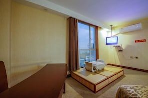 Una habitación de hotel con cama, una mesita, televisión y ventana con cortinas.