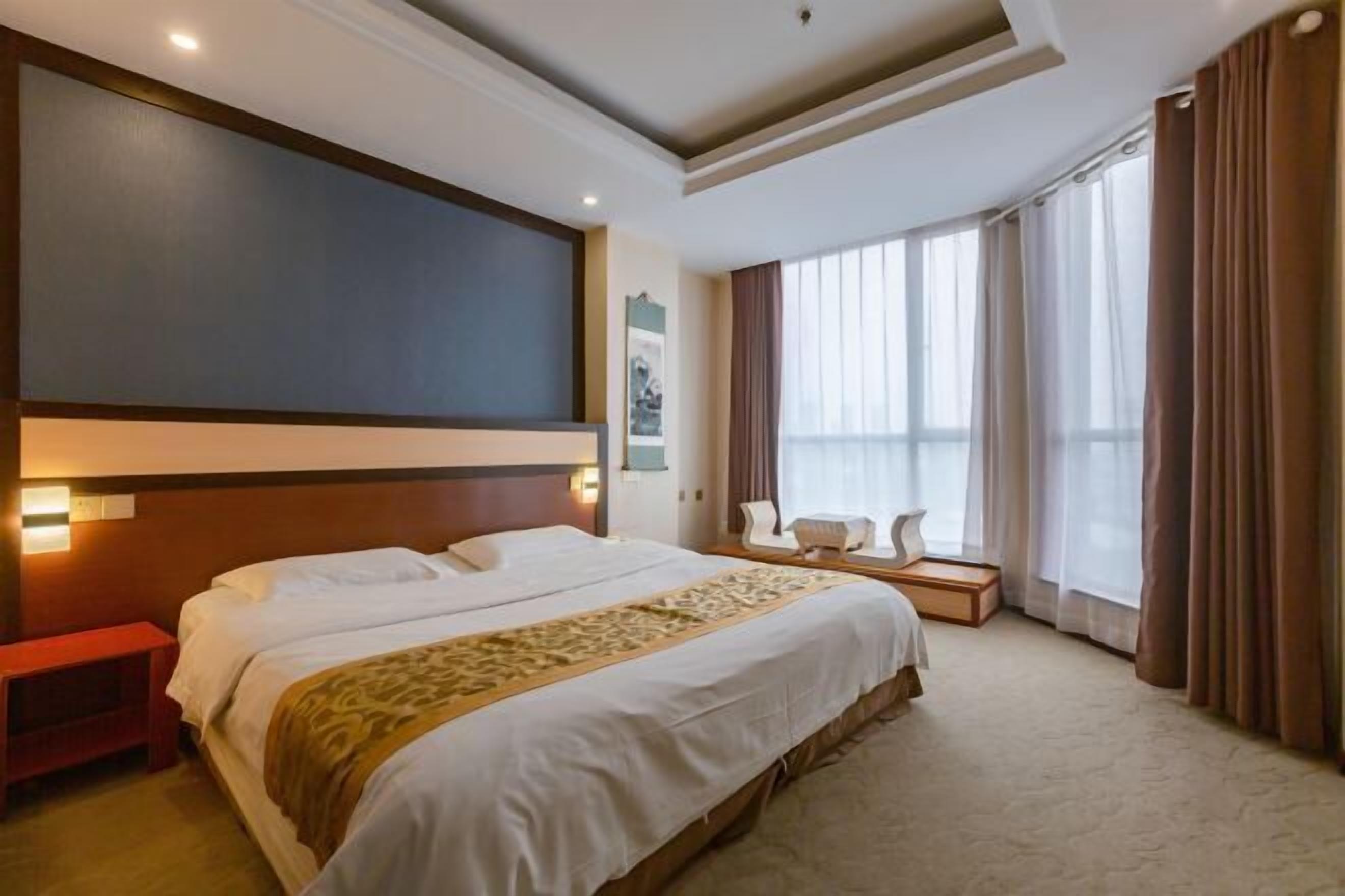 Quarto de hotel com uma cama grande, uma mesinha de cabeceira, uma cadeira e uma janela com cortinas.