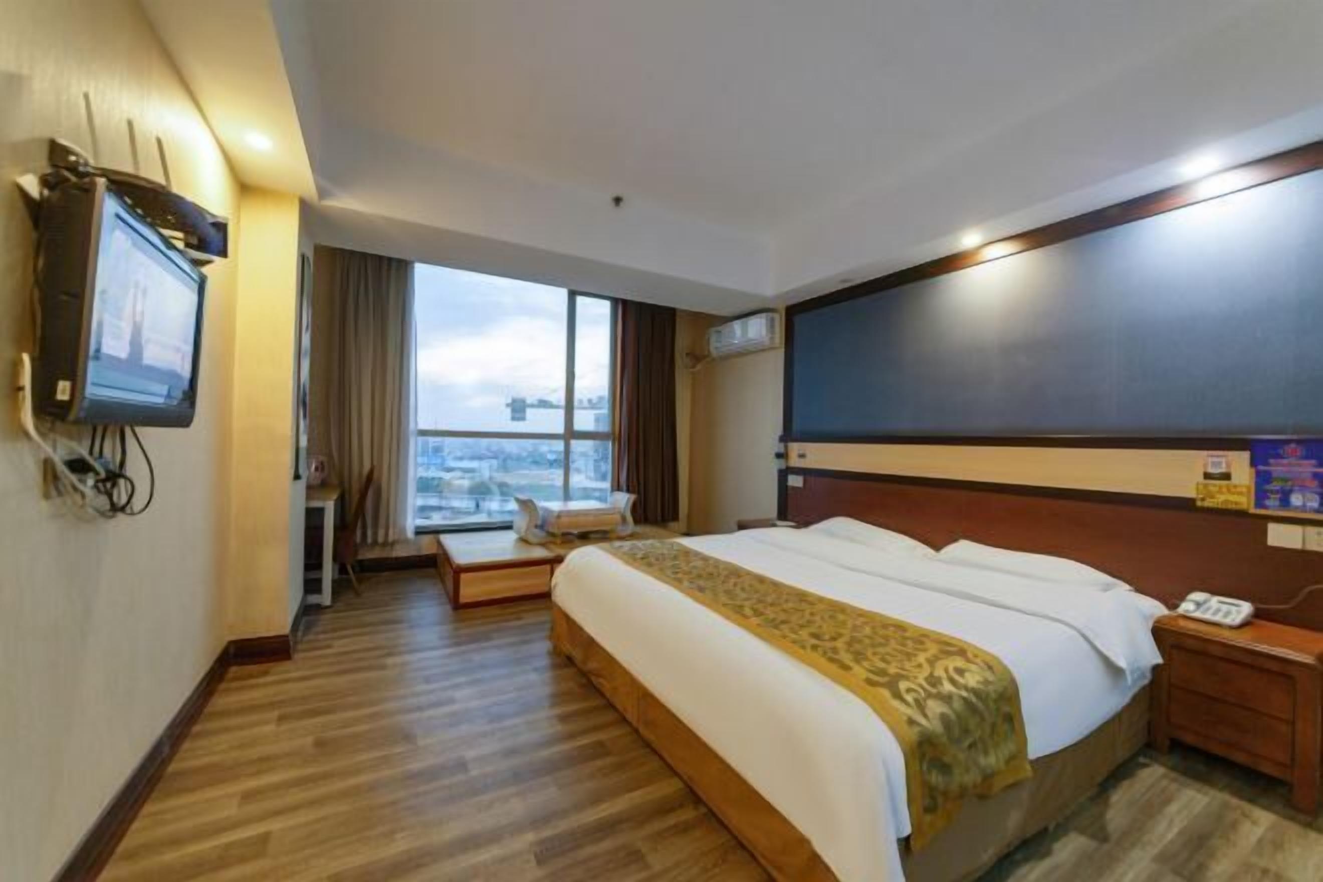 Quarto de hotel com cama grande, televisão na parede, janela com vista para a cidade e uma pequena mesa com cadeira.