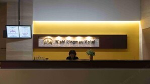 A hotel reception desk with a digital screen displaying information, a framed welcome sign, and a potted plant. - Nishi Kingmau Hotel (Changzhou)