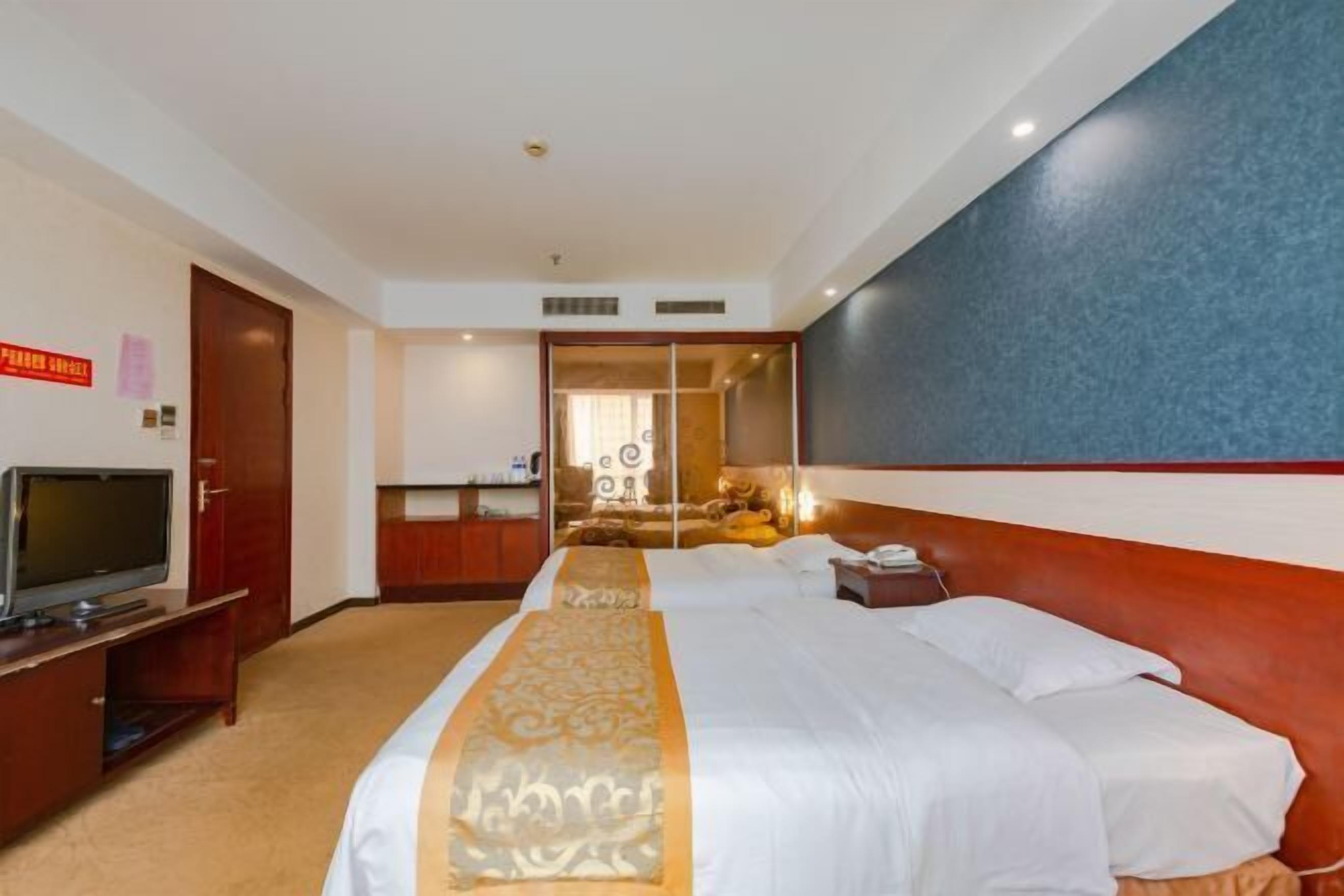 A hotel room with a large bed, a television on a stand, and a mirror on the wall.