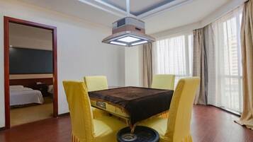 A hotel room with a bed, a table with yellow chairs, a ceiling light, and a window with curtains.