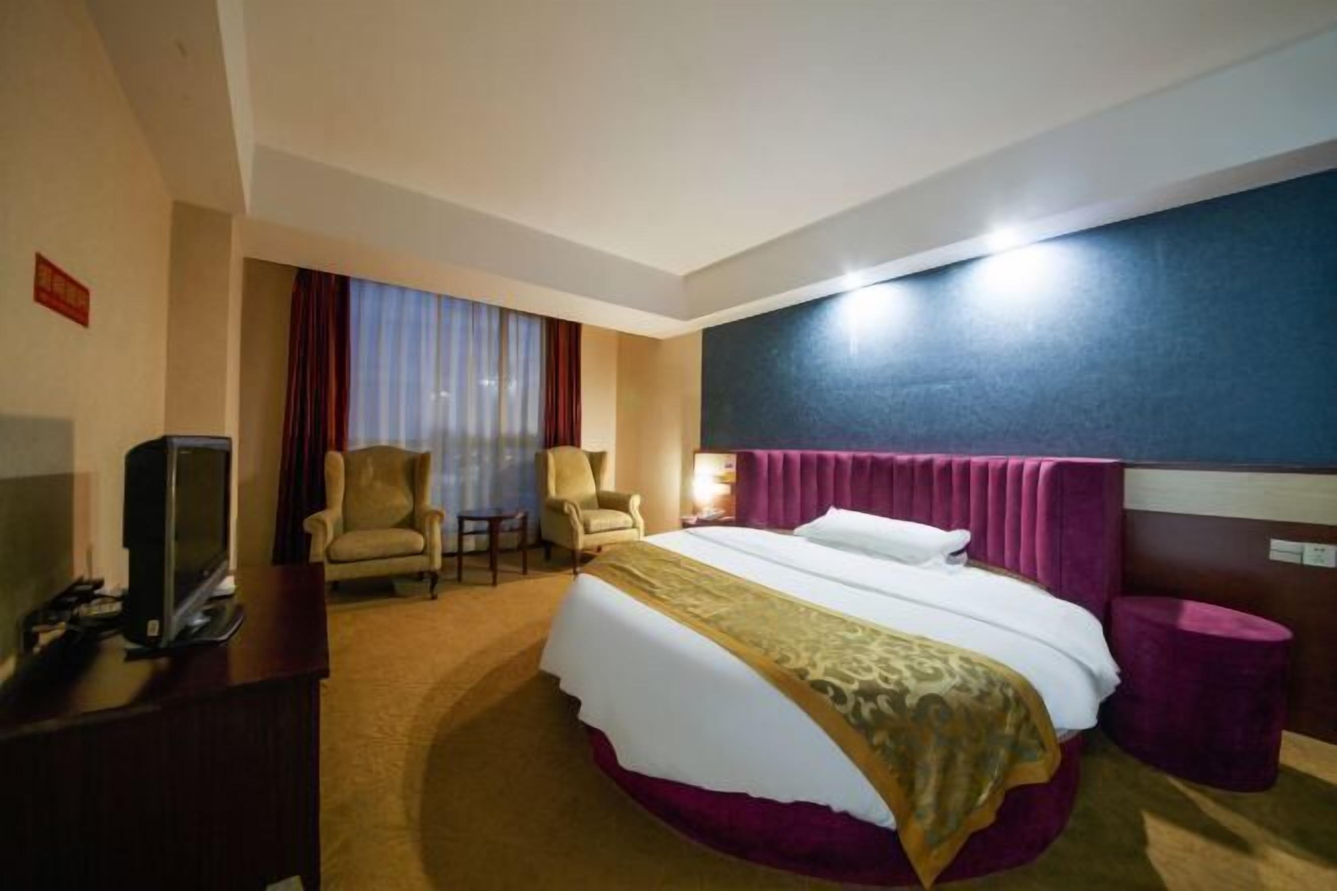 A hotel room with a bed, two armchairs, a television, and a desk.