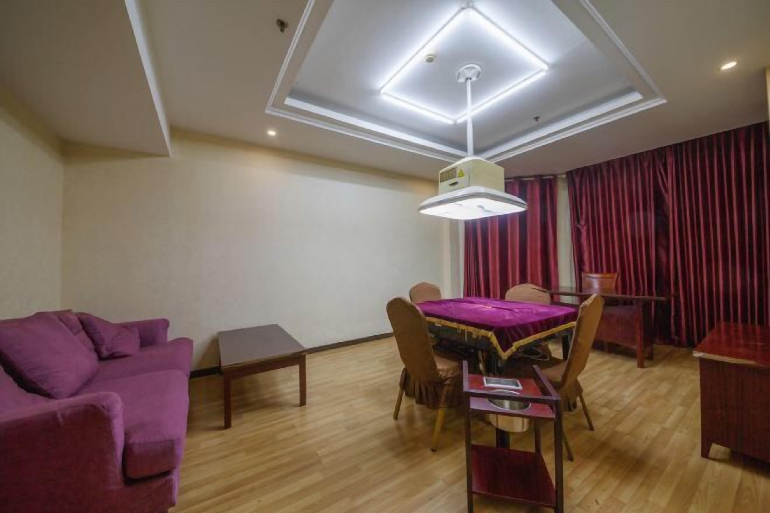 A modern hotel room with a dining area, a purple sofa, and a ceiling with recessed lighting.