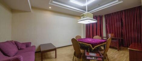 A modern hotel room with a dining area, a purple sofa, and a ceiling with recessed lighting.