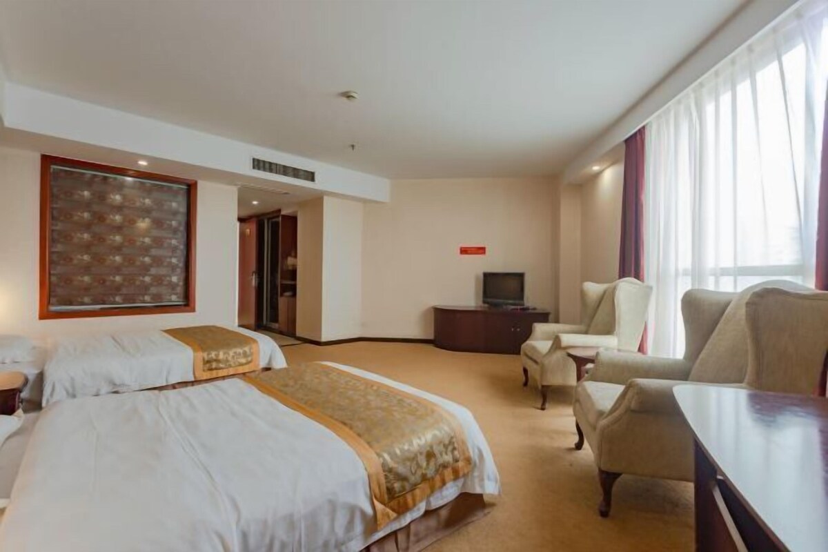 Ein Hotelzimmer mit zwei Betten, einem Fernseher, einem Schreibtisch und einem Sessel.